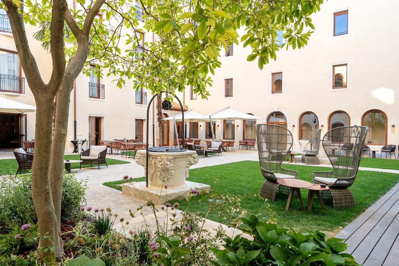 Ca' di Dio sleek suite with pale linen sofa, arched 13th-century window and a small outdoor terrace overlooking the lagoon