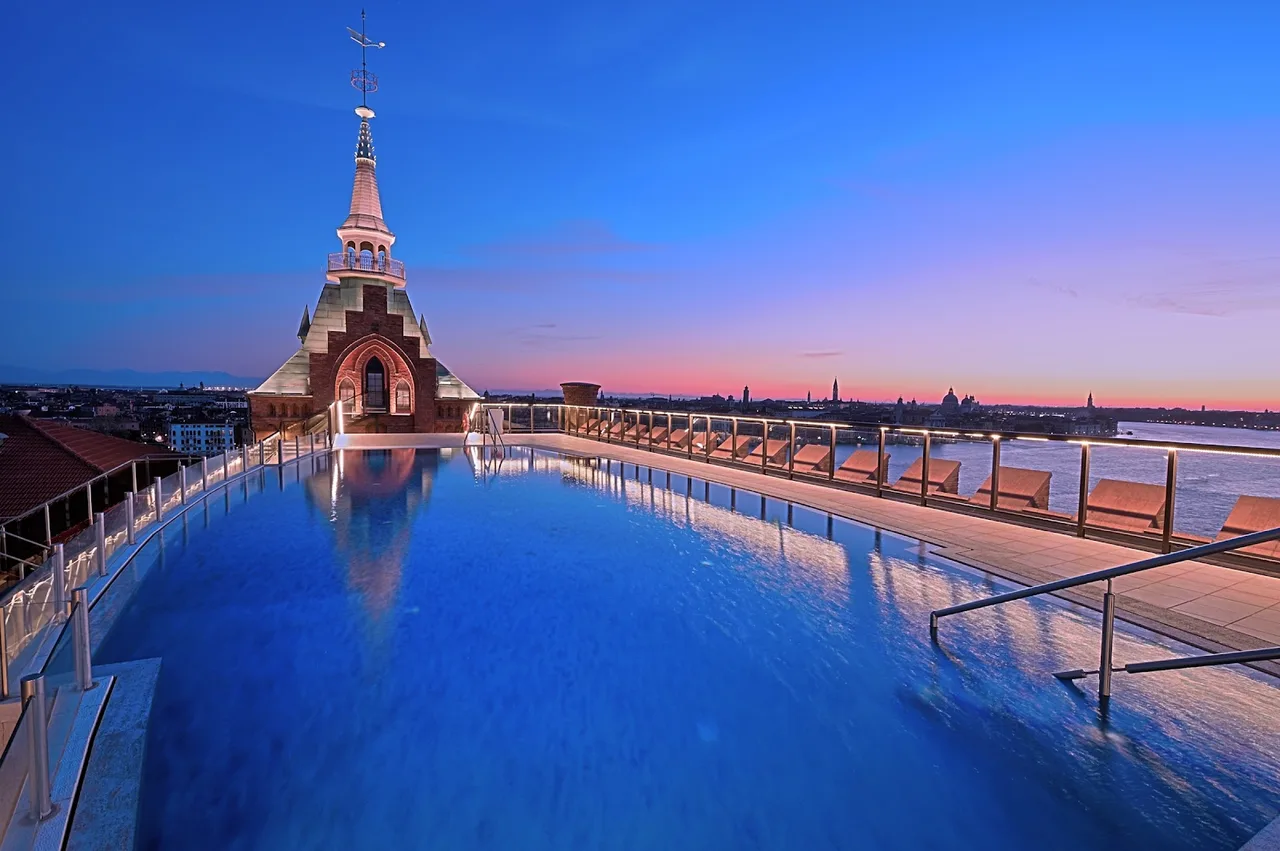 Hilton Molino Stucky Venice red-brick facade of the former flour mill on Giudecca, the rooftop pool deck visible against the San Marco skyline behind