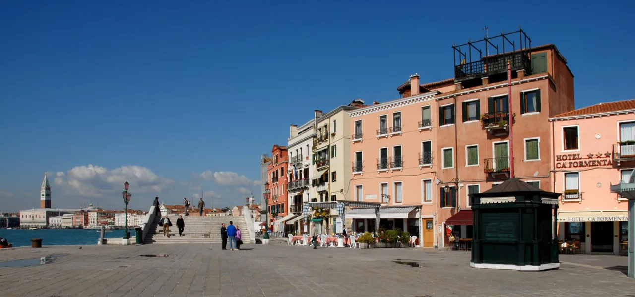 Hotel Cà Formenta entrance on Via Garibaldi with a brass plaque, awning with tables and the wide Venetian street continuing beyond