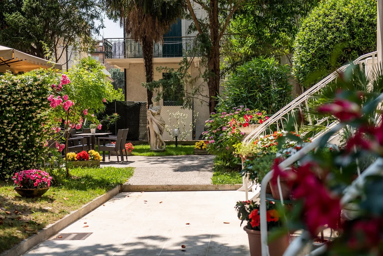 Hotel Villa delle Palme Venetian-style garden with palm trees, wooden loungers and a view down a quiet Lido residential street