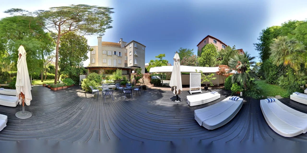 Hotel Villa Mabapa garden on Riviera San Nicolo with lagoon-facing loungers, a small restaurant terrace and palms overhanging the path