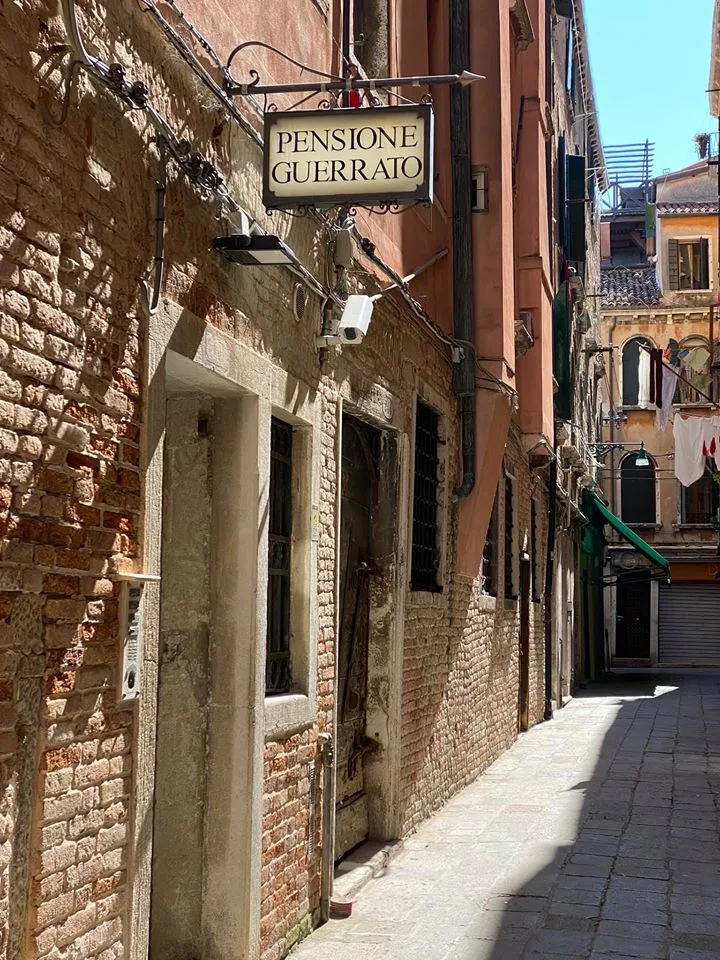 Pensione Guerrato 13th-century building facade on Calle Scimia with wrought-iron railings and a narrow Venetian street lantern